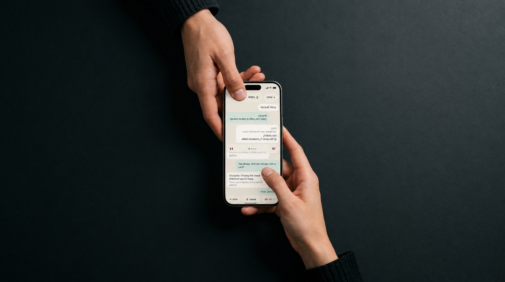 Two hands over a dark table, one phone between them: the near half of the screen in English for one person, the far half rotated and in Spanish for the other
